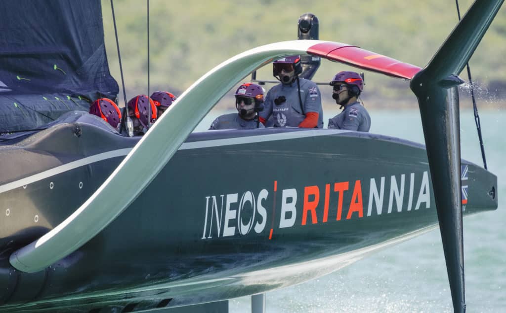 A closeup of the British AC75 Britannia, with skipper Ben Ainslie at the helm and visible behind the boat's large foil arm.