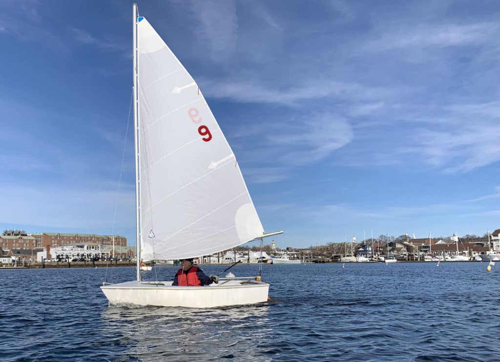 a white sailboat with white sail on Newport Harbor on a sunny winter day